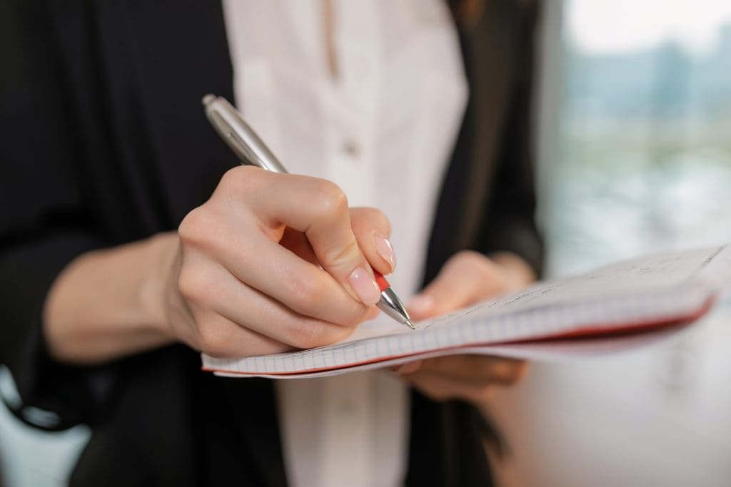 Close-up of a person writing with a pen on a notepad