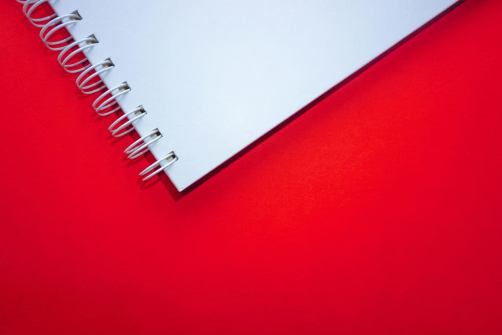 Close-up of the edge of a white spiral notebook against a red background