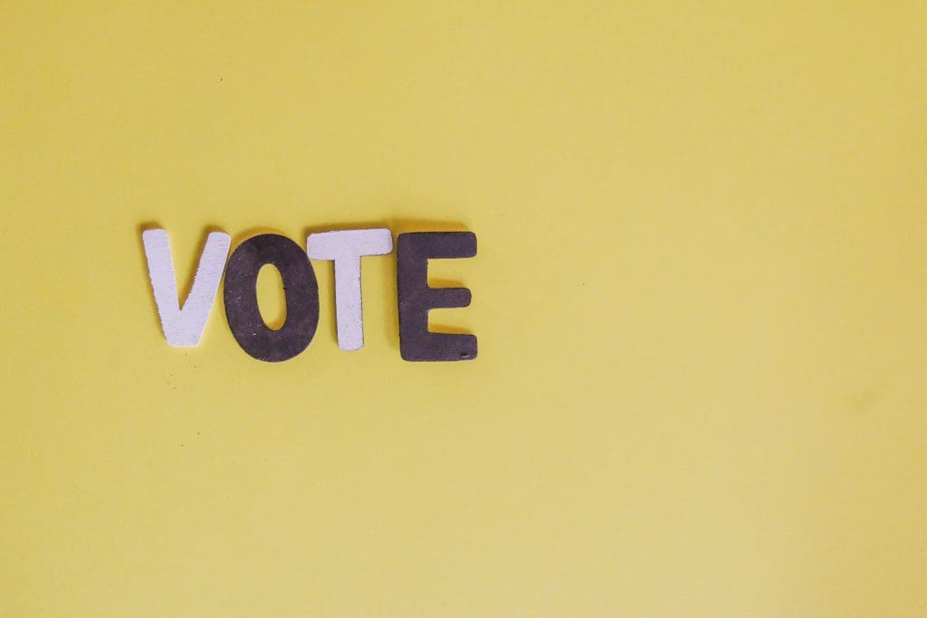 Pink and purple letters spelling "VOTE" against a yellow background